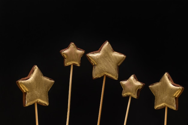 Goldfarbene sternförmige Lebkuchenplätzchen auf einem Stock auf einem Schwarzen