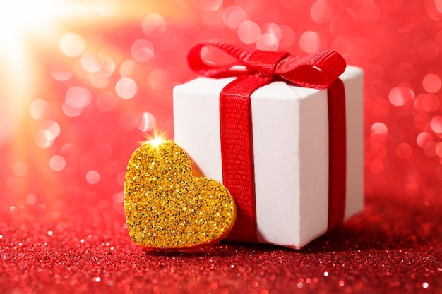 Goldherz und Geschenkbox auf glitzerndem rotem Hintergrund Konzept der Glückwünsche zum Valentinstag