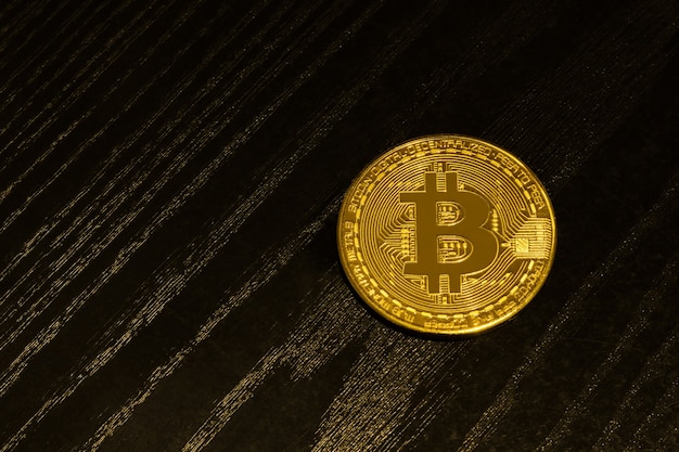 Goldmünze Bitcoin auf einem schwarzen Holzbrett