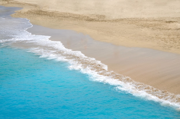 Goldsandstrand mit türkisfarbenen Meereswellen. Sommerzeit und Feiertagskonzepthintergrund. Abstrakter Seestückhintergrund. Draufsicht. Platz für Text.