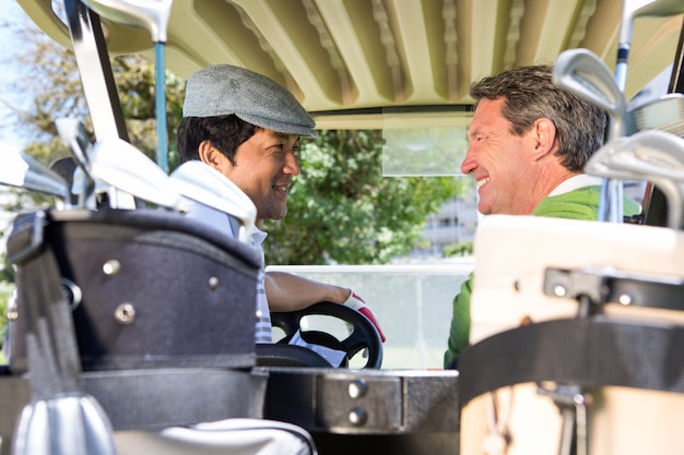 Golf amigos manejando en su buggy de golf sonriendo el uno al otro