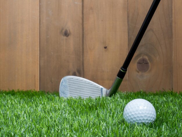 Golf y pelota sobre hierba verde y fondo de madera