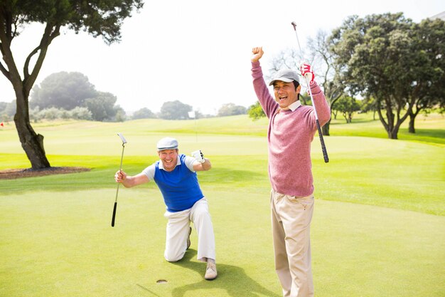 Golf spielende Freunde, die auf dem Übungsgrün am Golfplatz zujubeln