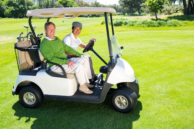 Golf spielende Freunde, die in ihren Golfbuggy lächelt an der Kamera fahren