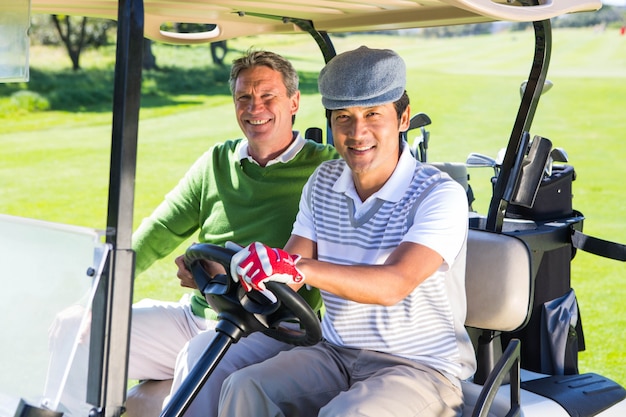 Golf spielende Freunde, die in ihren Golfbuggy lächelt an der Kamera fahren