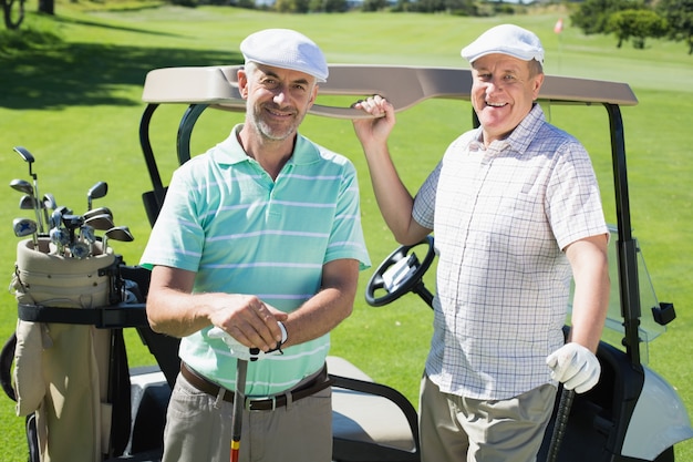 Golf spielende Freunde, die neben ihrem Buggy lächelt an der Kamera stehen