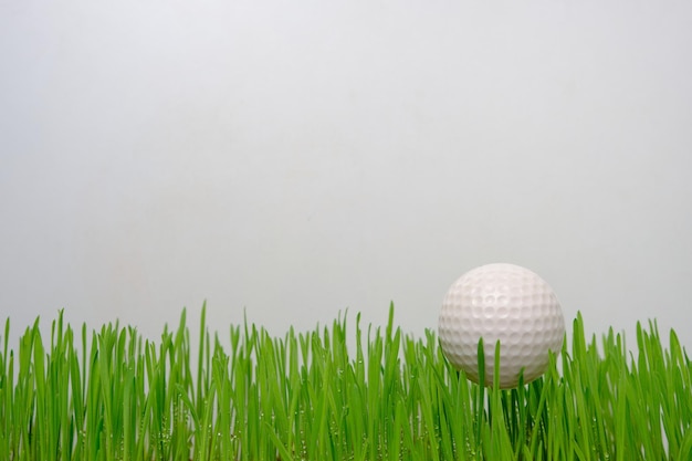 Golfball auf grünem Rasen auf weißem Hintergrund.