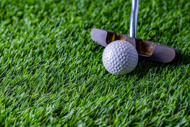 Golfball mit Putter auf grünem Gras