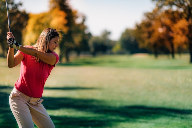 Golfende Dame in einem Golfschwung, der von hinten geschossen wird