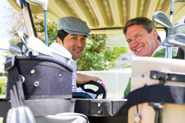 Golfing amigos conduciendo en su carrito de golf sonriendo a la cámara