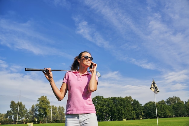 Golfista alegre con un palo de golf hablando por el teléfono inteligente