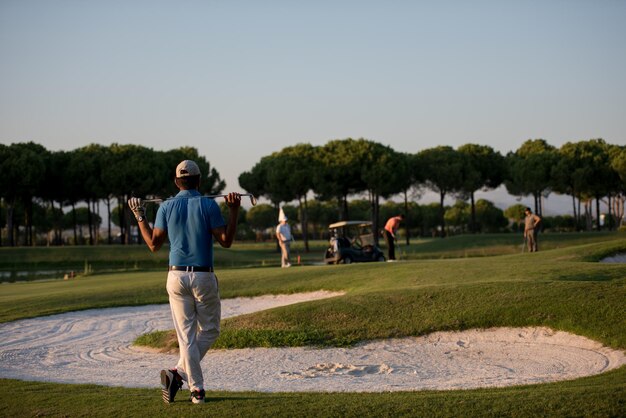 golfista desde atrás mirando a la pelota y al hoyo en la distancia, hermoso retrato de jugador de golf del medio oriente desde atrás con hermosa puesta de sol en el fondo