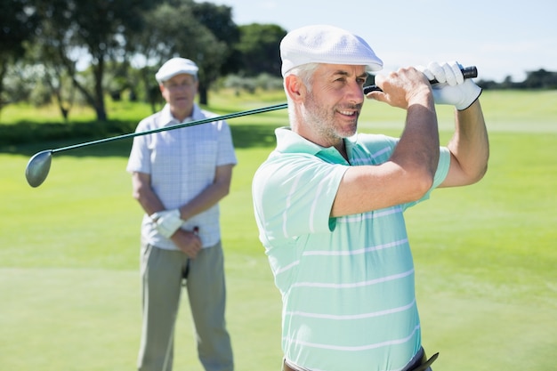 Golfista balanceando su club con un amigo detrás de él