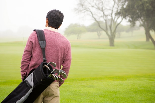 Golfista caminando y sosteniendo sus bolsas de golf