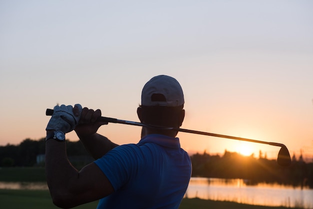 golfista golpeando tiro largo con conductor en curso en la hermosa puesta de sol