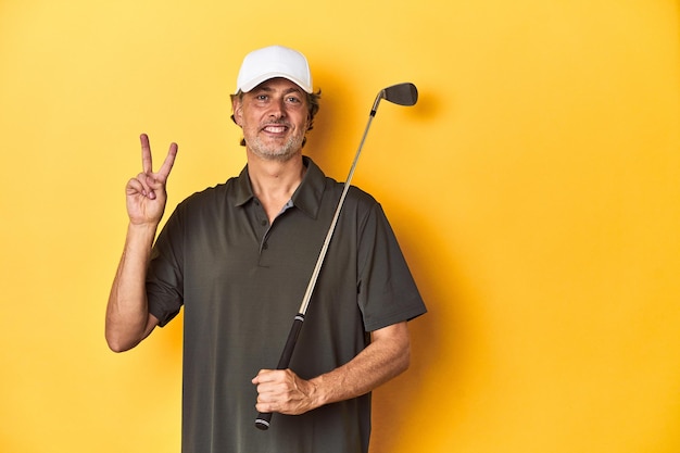 Golfista de mediana edad con palo y gorra en amarillo que muestra el número dos con los dedos