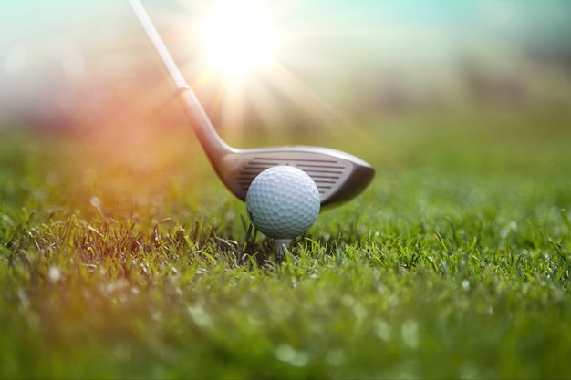 Golfista poniendo una pelota de golf en el campo de golf verde, destello de lente en la puesta de sol por la noche.