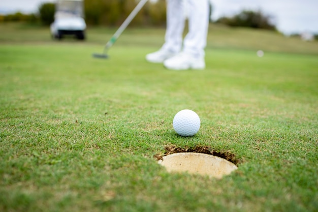 Golfista profesional irreconocible que pone la bola en el hoyo del campo de golf.