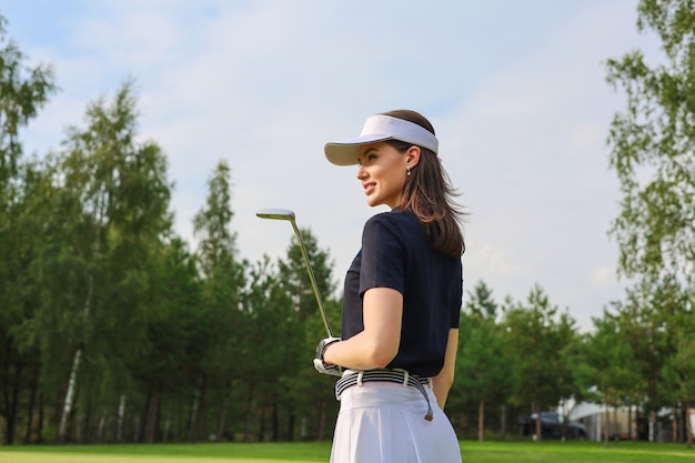 Golfista profesional sosteniendo el club de golf en el campo y mirando a otro lado. Mujer joven de pie en el campo de golf en un día soleado.