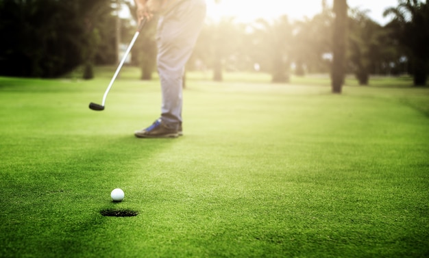 El golfista que pone la bola de golf se acerca al hoyo del golf en el golf verde