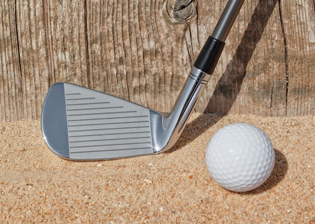 Golfschläger und Ball unterstützen Holznahaufnahme auf dem Sand.