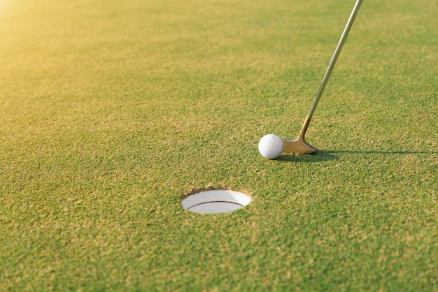 Golfspieler am Puttinggrün, der Golfball in ein Loch schlägt. Schließen Sie oben am Golfball und am Putter.