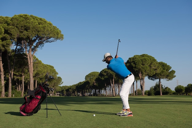 Golfspieler, der am schönen Morgen mit Sonneneruption im Hintergrund mit Schläger auf Kurs schlägt