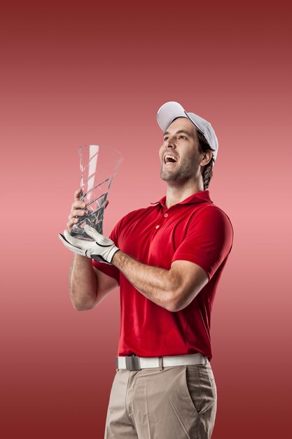 Golfspieler in einem roten Hemd, das mit einer Glastrophäe in seinen Händen auf einem roten Hintergrund feiert.