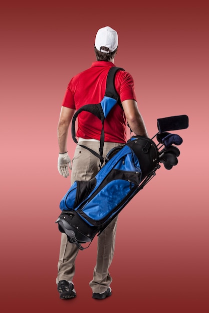 Golfspieler in einem roten Hemd, das mit einer Tasche der Golfschläger auf seinem Rücken auf einem roten Hintergrund geht.