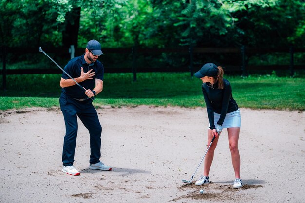 Golfunterricht Junge Frau, die einen Golfunterricht hat, der vom Sandbunker spielt