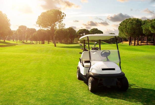 Golfwagen im Fairway des Golfplatzes mit grünem Rasenfeld und bewölktem Himmel und Bäumen beim Sonnenuntergang