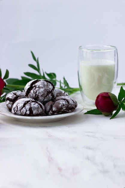 Golosinas en una mesa blanca Chocolate cracks cookies un vaso de leche y peonías