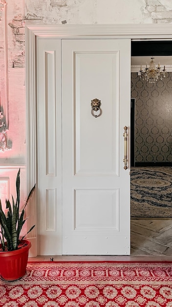 Golpeador de puerta dorado adornado en puerta blanca con alfombra de patrón rojo