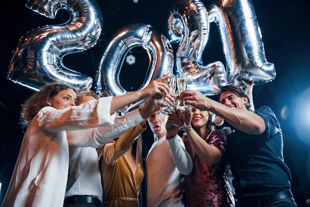 Golpeando vasos. Alegre grupo de personas con bebidas y globos en las manos celebrando el nuevo año 2021.