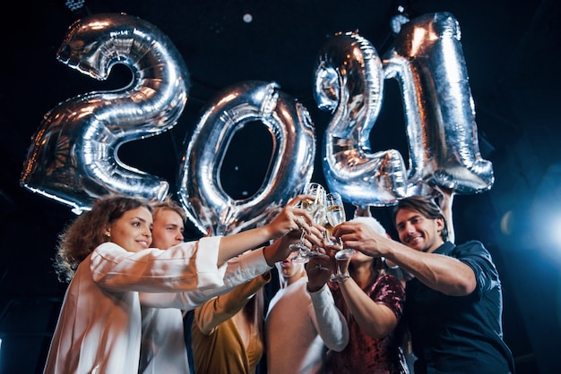 Foto golpeando vasos. alegre grupo de personas con bebidas y globos en las manos celebrando el nuevo año 2021.