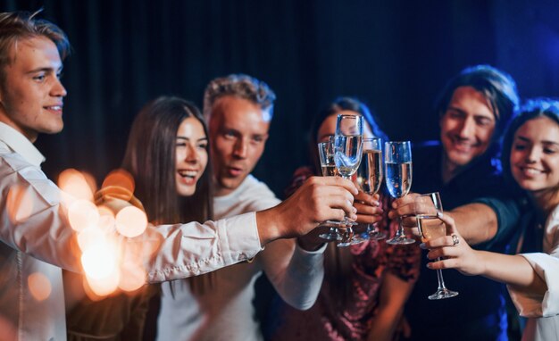Golpeando vasos. Grupo de amigos alegres celebrando el año nuevo en el interior con bebidas en las manos.