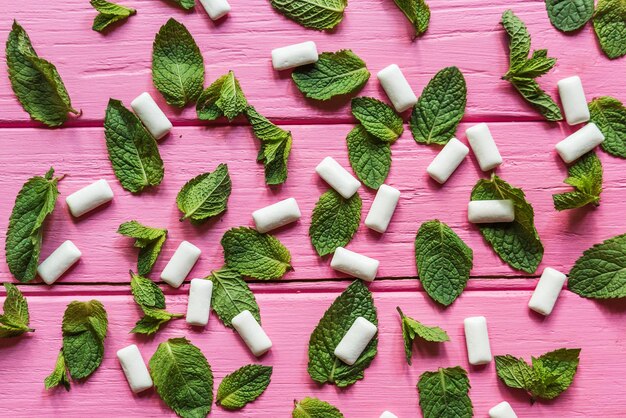 Goma de menta y hojas de menta sobre fondo de madera rosa