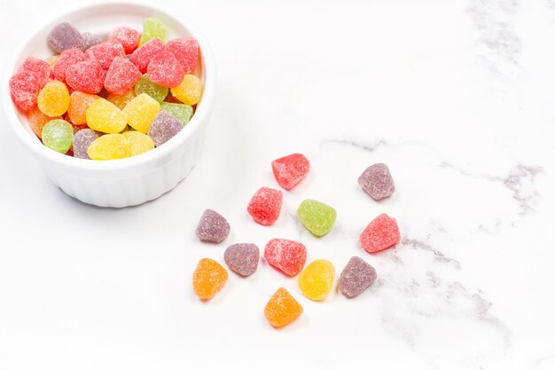 Foto gomitas de colores en un recipiente blanco y en un mostrador de cocina de mármol