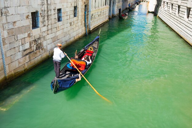 Gôndola com turistas no canal estreito entre edifícios antigos. Veneza, Itália