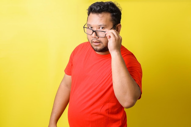 El gordo asiático con camiseta roja usa anteojos tiene curiosidad por algo y se ve seriamente aislado