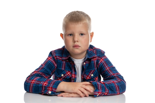 El gordo está sentado a la mesa. Colegial con una camisa a cuadros. De vuelta a la escuela. Aislado. De cerca.