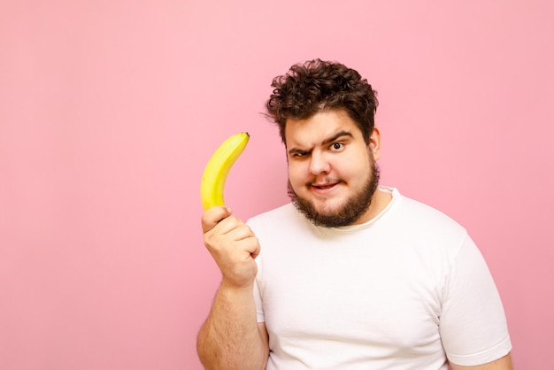 Foto un gordo gracioso con una camiseta blanca sostiene un plátano en la mano