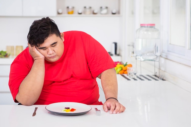 El gordo joven parece aburrido de comer ensalada