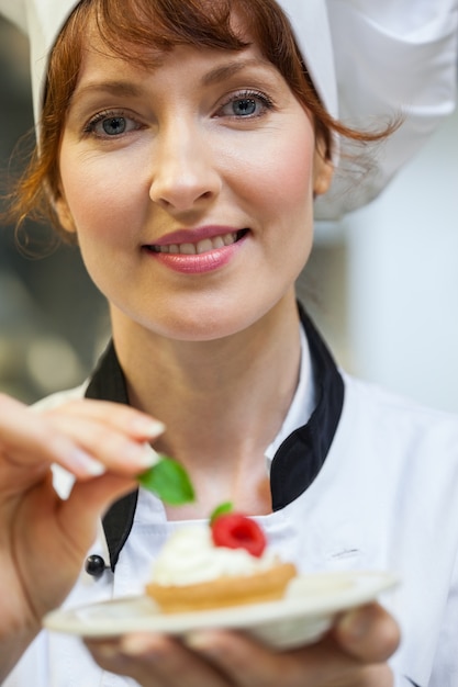 Gorgeous chef chefe colocando folha de hortelã no pequeno bolo no prato