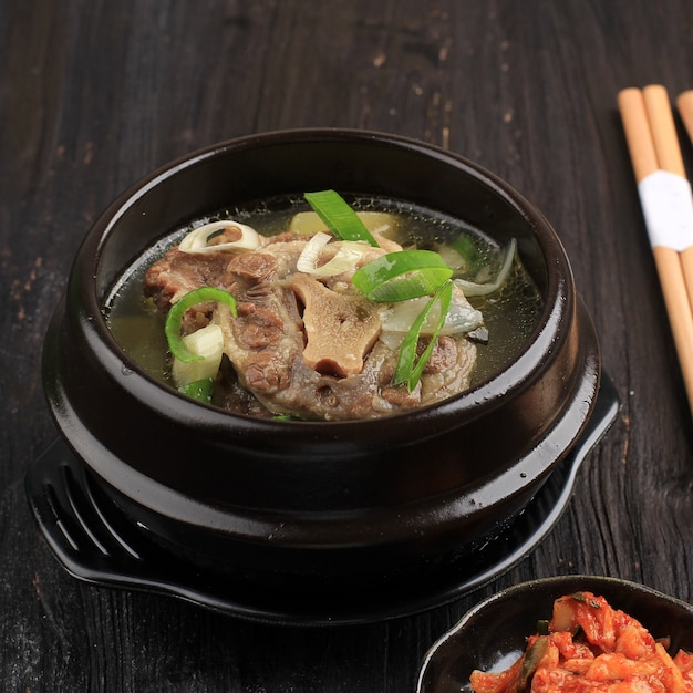 Gori Gomtang (Sokkori Gomtang) oder koreanische Rinder-Ochsenschwanz-Eintopfsuppe, serviert in der schwarzen koreanischen Schüssel mit Kimchi und geschnittener grüner Zwiebel