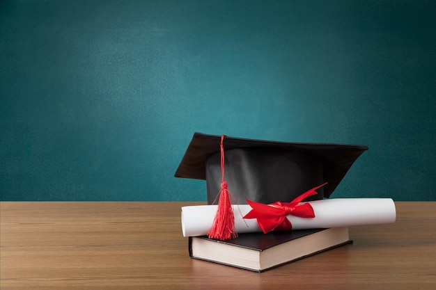 Gorra académica, diploma de graduación y un libro frente a la pizarra verde