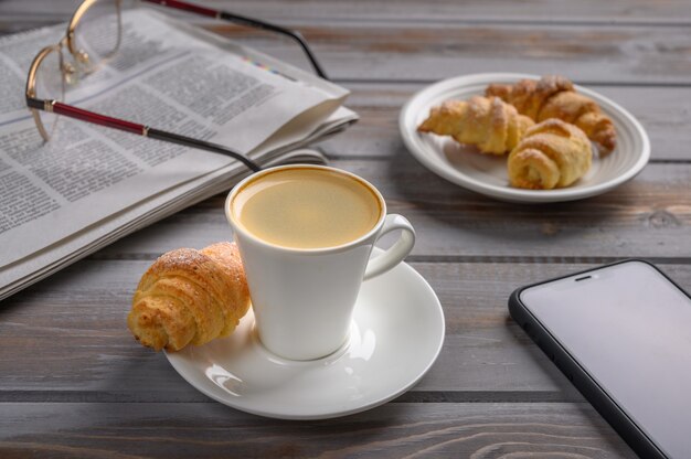 Gorra de café y bagels de galletas caseras en la superficie de madera cerca del periódico del teléfono inteligente y gafas