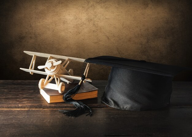 Gorra de graduación, sombrero con avión de juguete de madera en mesa de madera