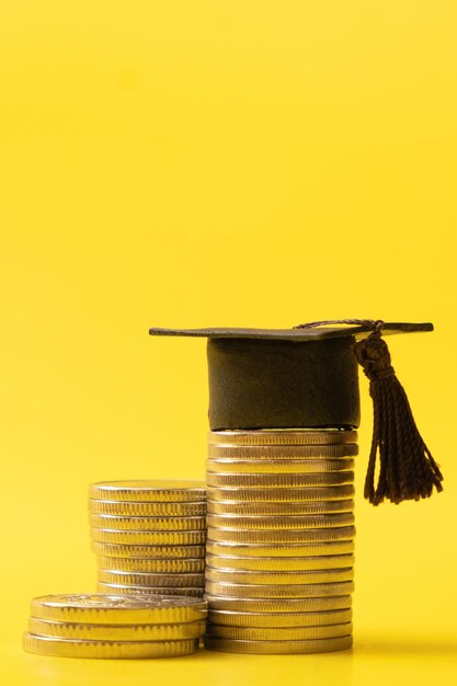 Gorra graduada con monedas sobre fondo amarillo Concepto de ahorro para la educación