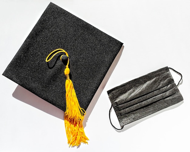 Foto gorra graduada negra con borla amarilla y mascarilla protectora sobre fondo blanco